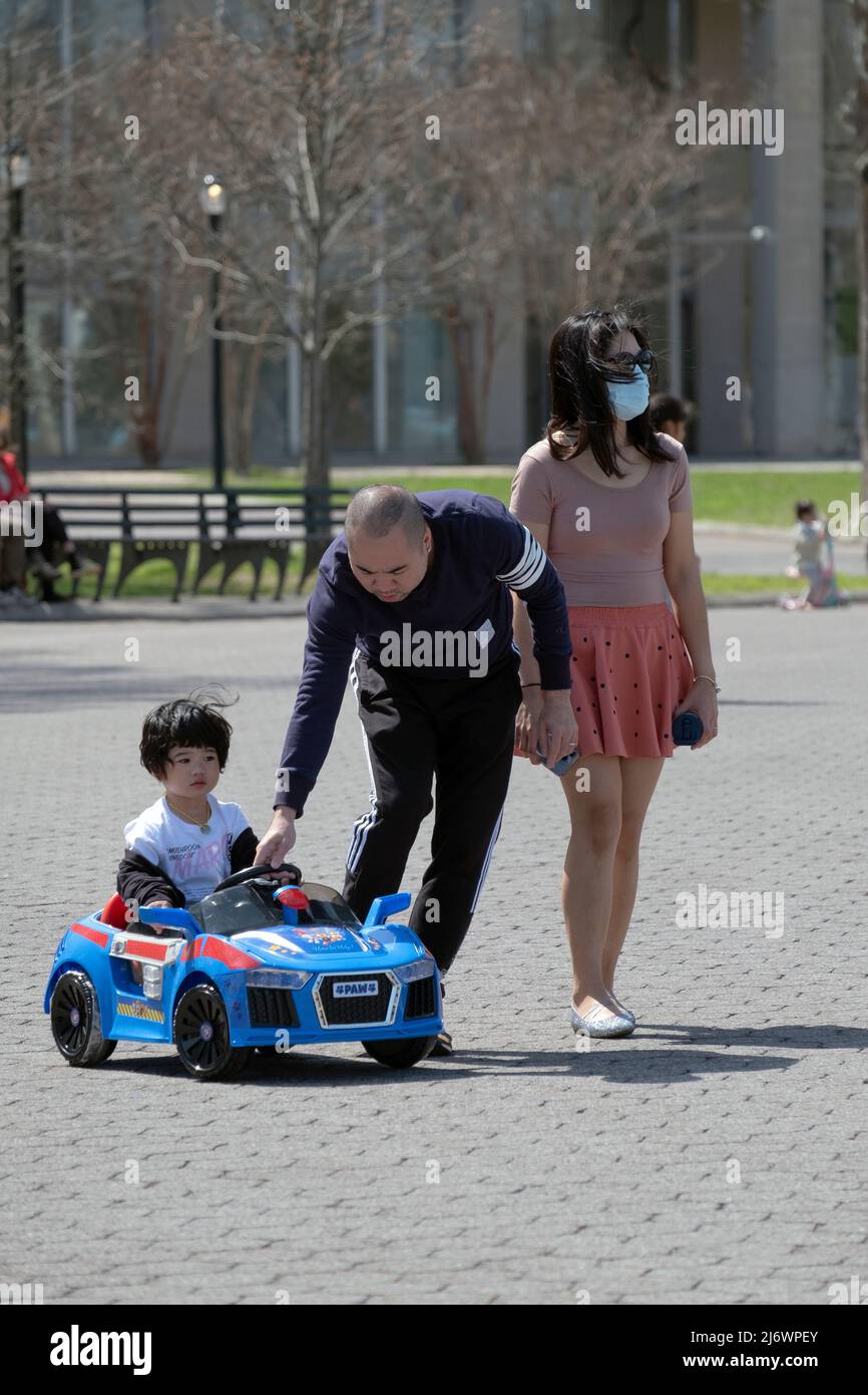 On a mild spring day a family take their son out for a spin in his electric car. in a park in Queens, New York. Stock Photo