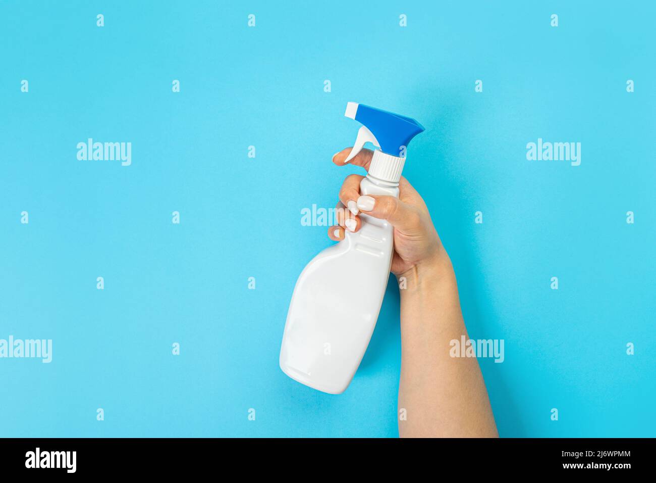 Housewife's hand holds a spray with cleaning agent on a blue background