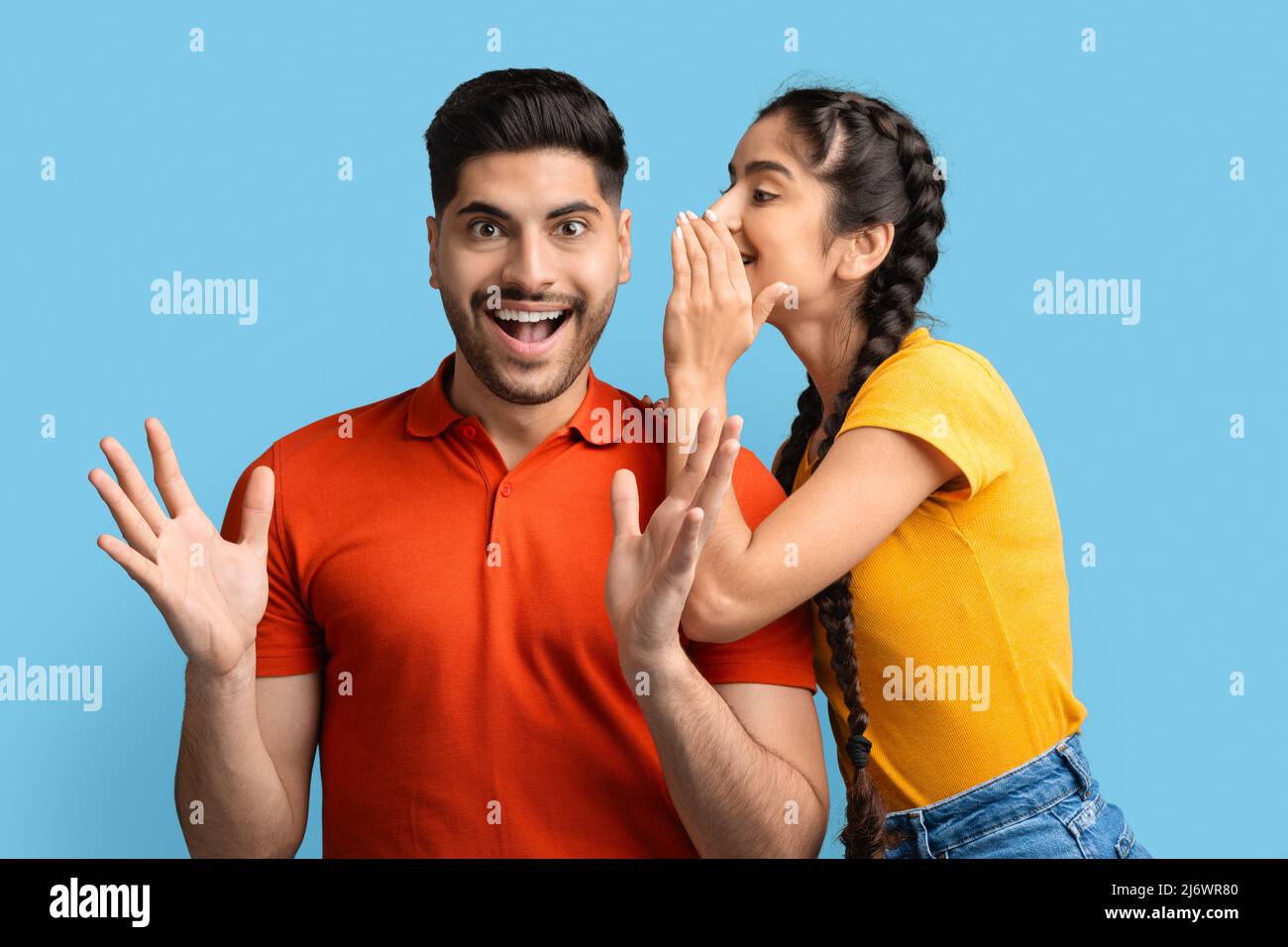 Cheerful Arab Woman Sharing Secrets With Excited Boyfriend, Whispering To His Ear Stock Photo