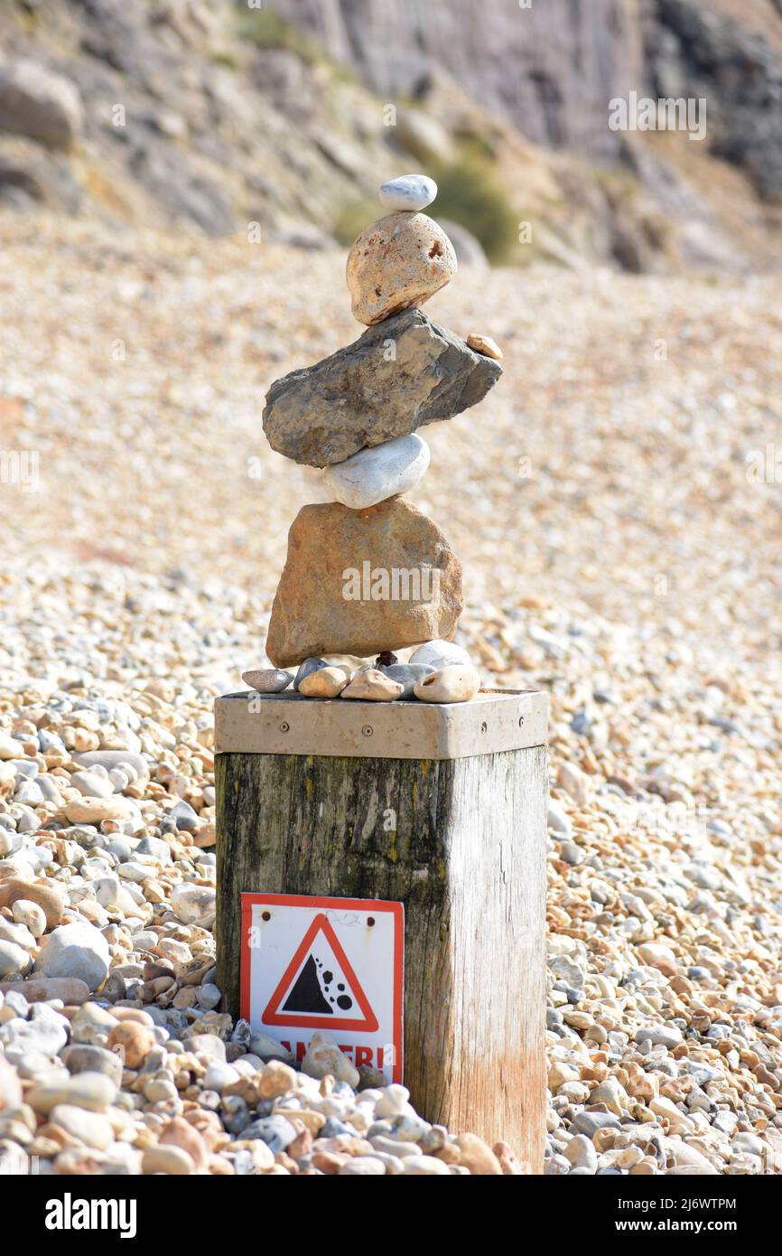Stone balancing on a sunny rocky beach with a hazard warning sign Stock Photo