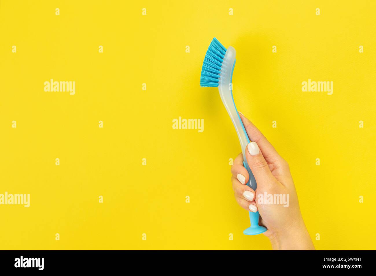 The housewife's hand holds a cleaning brush. Empty space for text or logo on a yellow background. Early spring or regular cleaning. Cleaning and clean Stock Photo