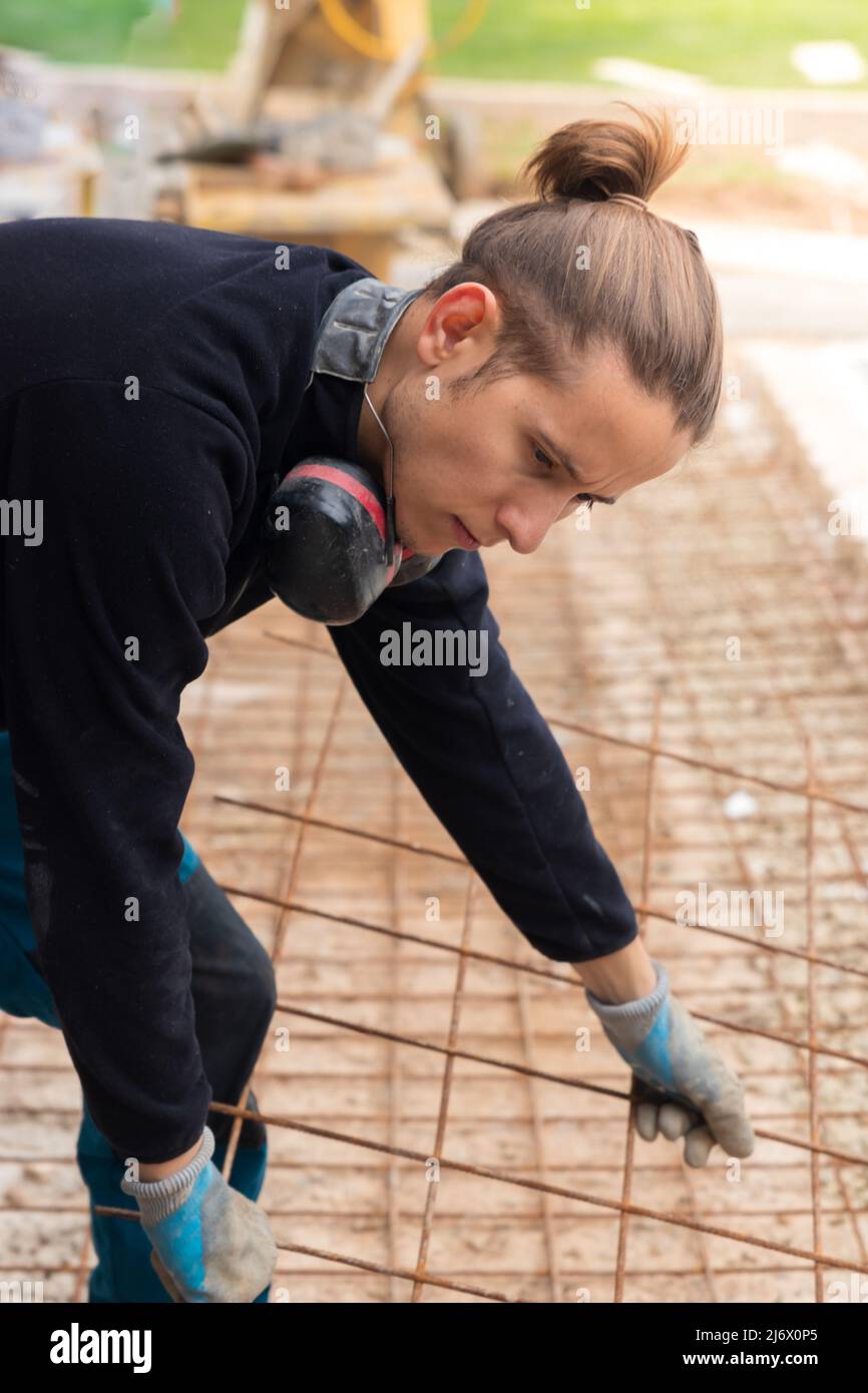 Young hipster man apprentice working in construction placing rusty iron mesh grid on the floor Stock Photo