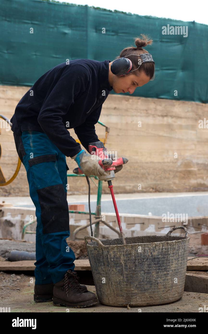 Young working man using drill mixing machine construction products with anti-sound headphones on in a construction site Stock Photo
