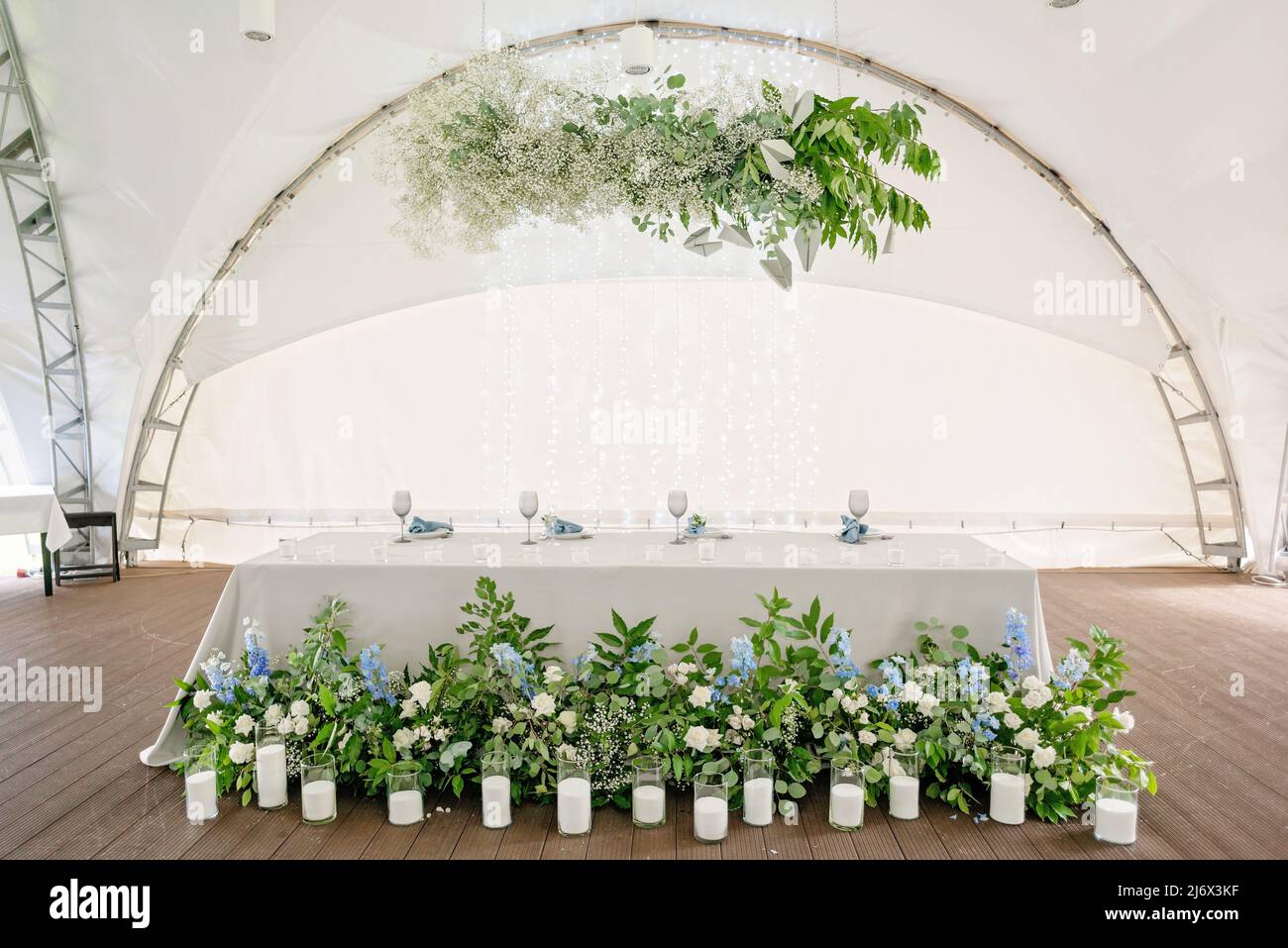 Wedding presidium in restaurant. Banquet table for newlyweds with flowers, greenery, candles and garland ligths. Lush floral arrangement. Luxury weddi Stock Photo
