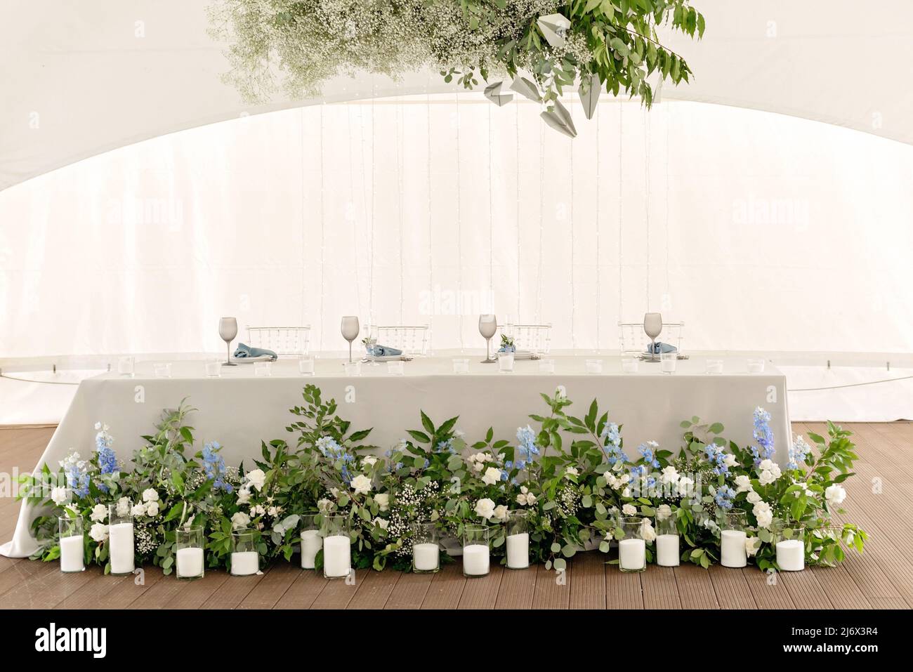 Wedding presidium in restaurant. Banquet table for newlyweds with flowers, greenery, candles and garland ligths. Lush floral arrangement. Luxury weddi Stock Photo