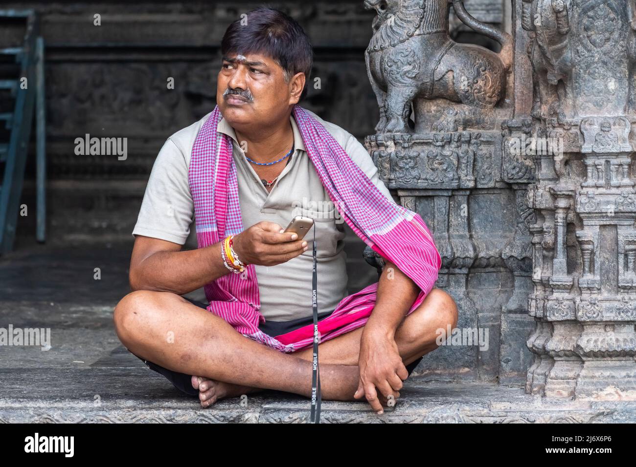Vellore, Tamil Nadu, India - September 2018: An Indian man wearing a red stole sitting cross legged at an ancient Hindu temple in the Vellore fort. Stock Photo