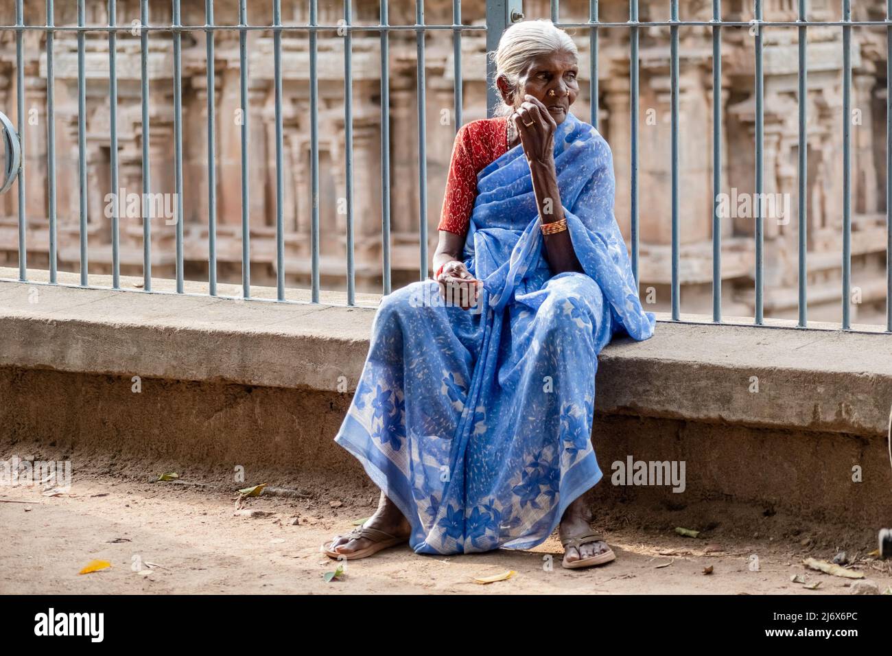 Vellore, Tamil Nadu, India - September 2018: Candid portrait of an elderly Indian woman wearing a blue sari sitting outside an ancient Hindu temple in Stock Photo