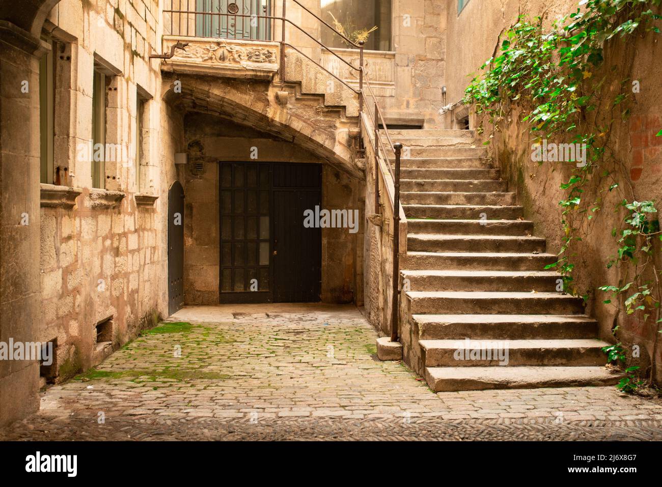 European courtyard with ancient architecture of stone, stairs, entrance door with ivy seen from Girona Spain. Stock Photo