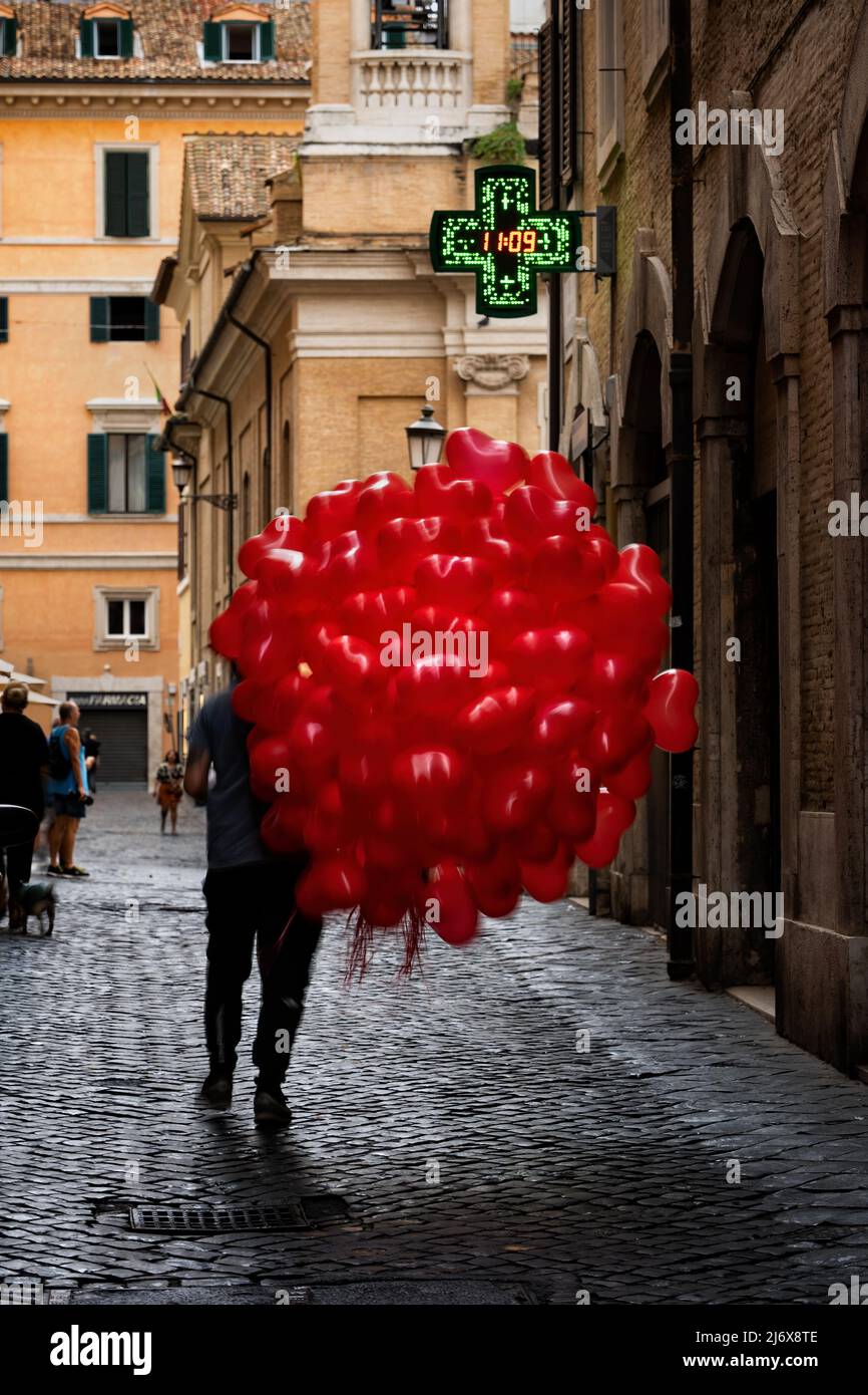 Man on cobblestone street walking with a bunch of red balloons in shape of heart in city of Rome, Italy. Stock Photo