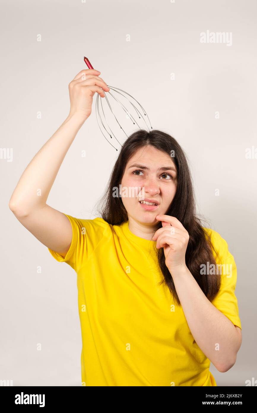 A woman with a disgruntled grimace on her face massages her head with a massager. Stock Photo