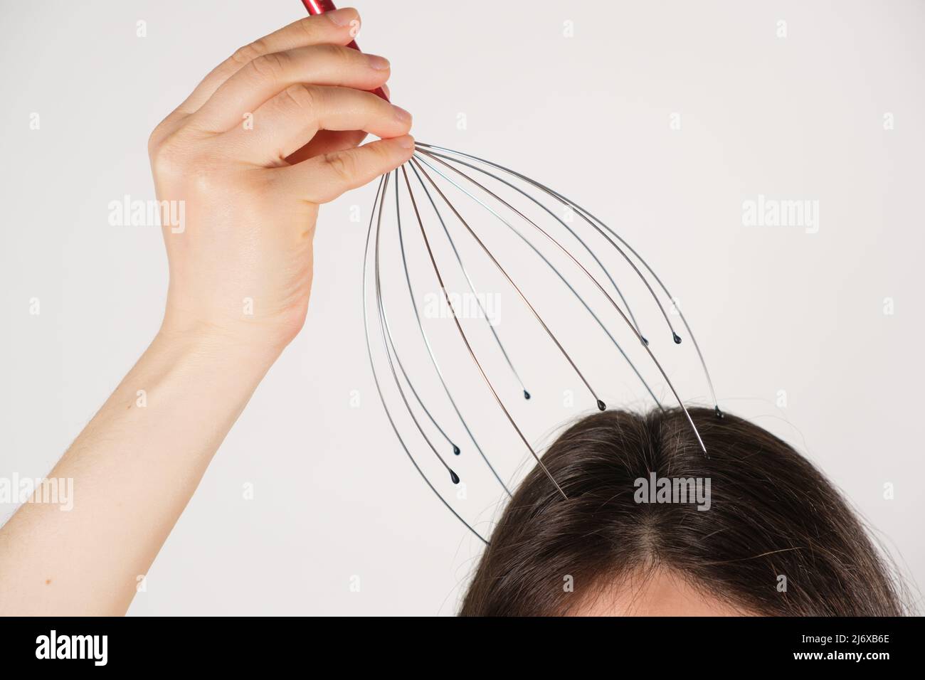 A woman with a metal flexible massager for self-massage of the head on a white background, copy the place for the text Stock Photo