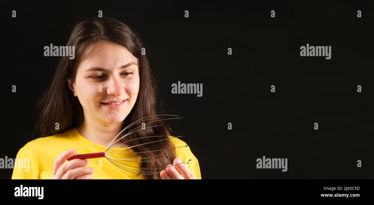 A woman with a metal flexible massager for self-massage of the head on a black background. Banner with place for text. Stock Photo