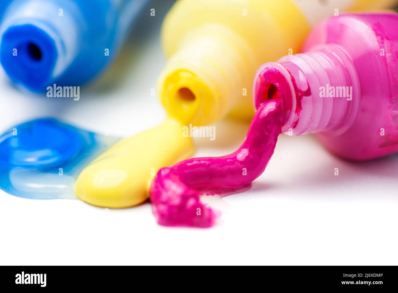 Close-up of three open tubes with magenta, yellow and blue artist paints spilling out on a white background. Stock Photo