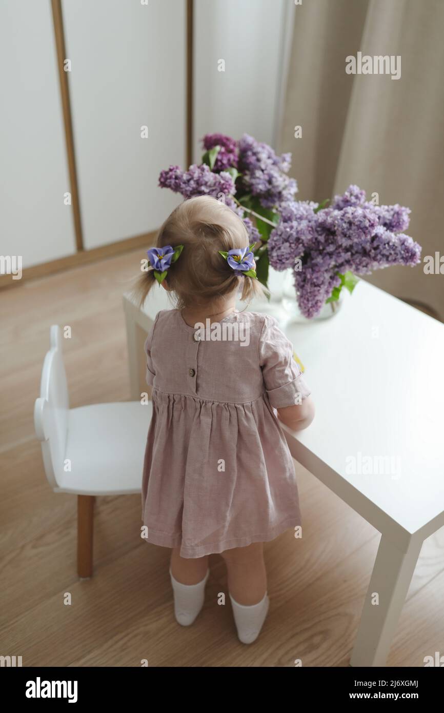 little girl in a pink dress at home with a bouquet of fragrant lilacs ...