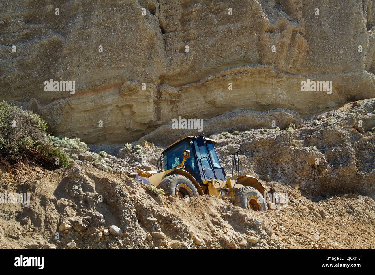 Yellow excavator working on repairing a road in the mountains Stock Photo