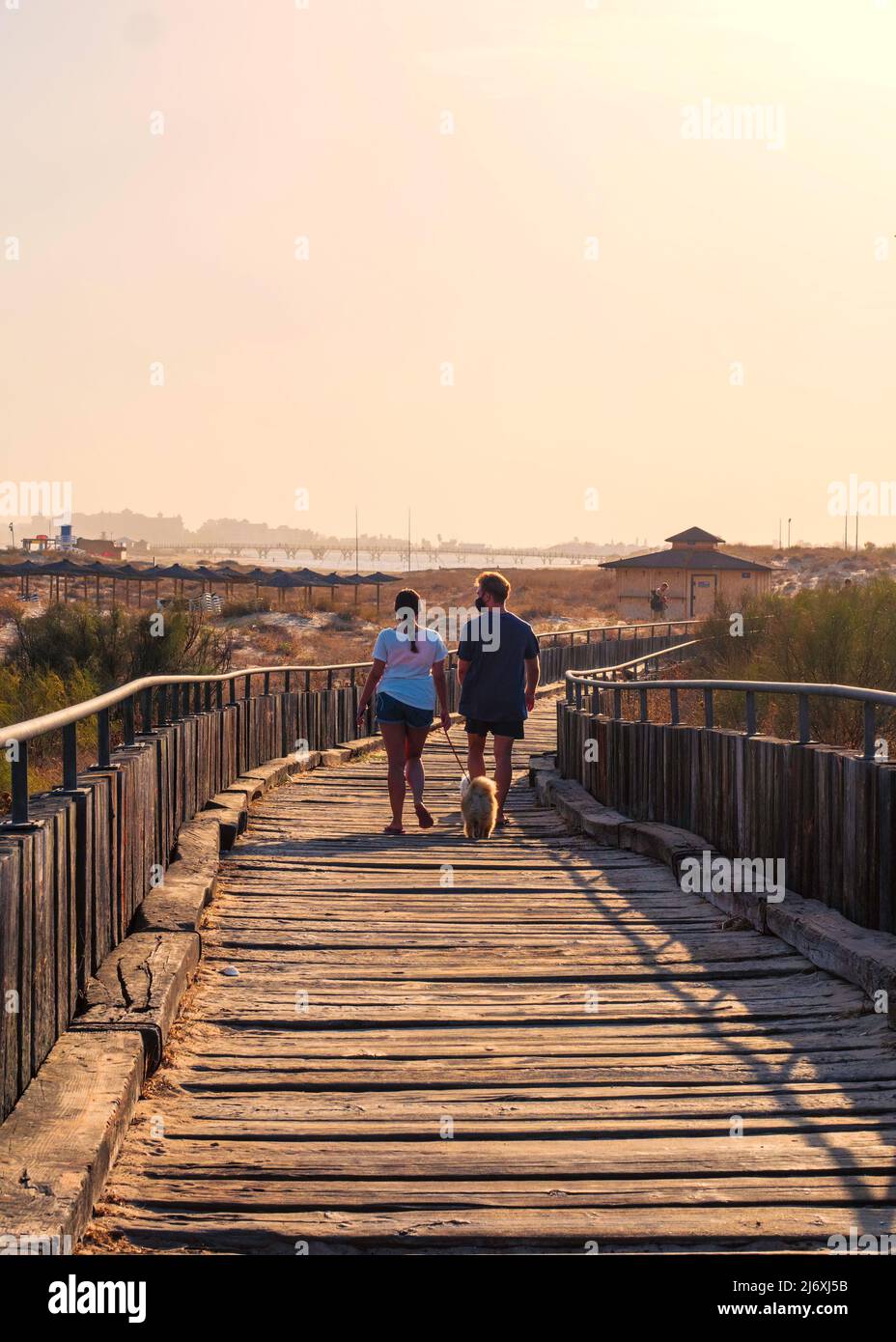A couple walks along a wooden path between the sand of the beach of Isla Cristina Stock Photo