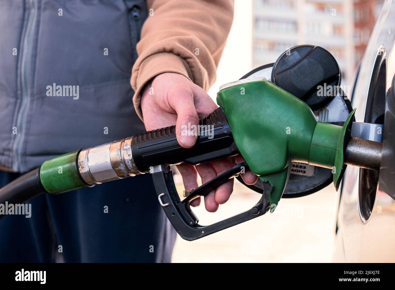 A gray car is refueling at a gas station. The man inserted a fuel pistol into the tank. Stock Photo