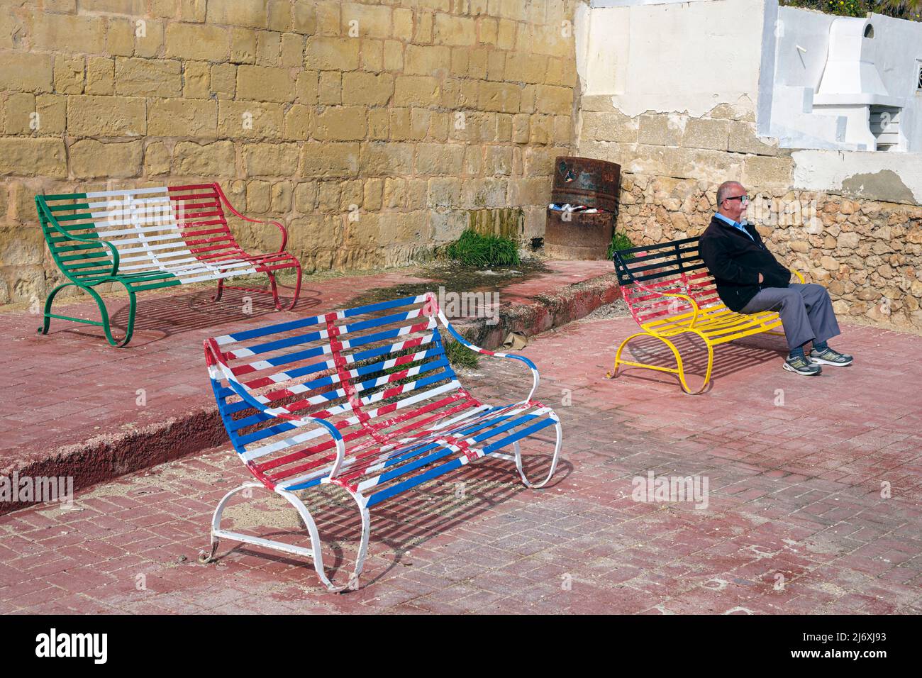 Benches painted in the colours of various national flags on the seafront at Qawra, Malta Stock Photo