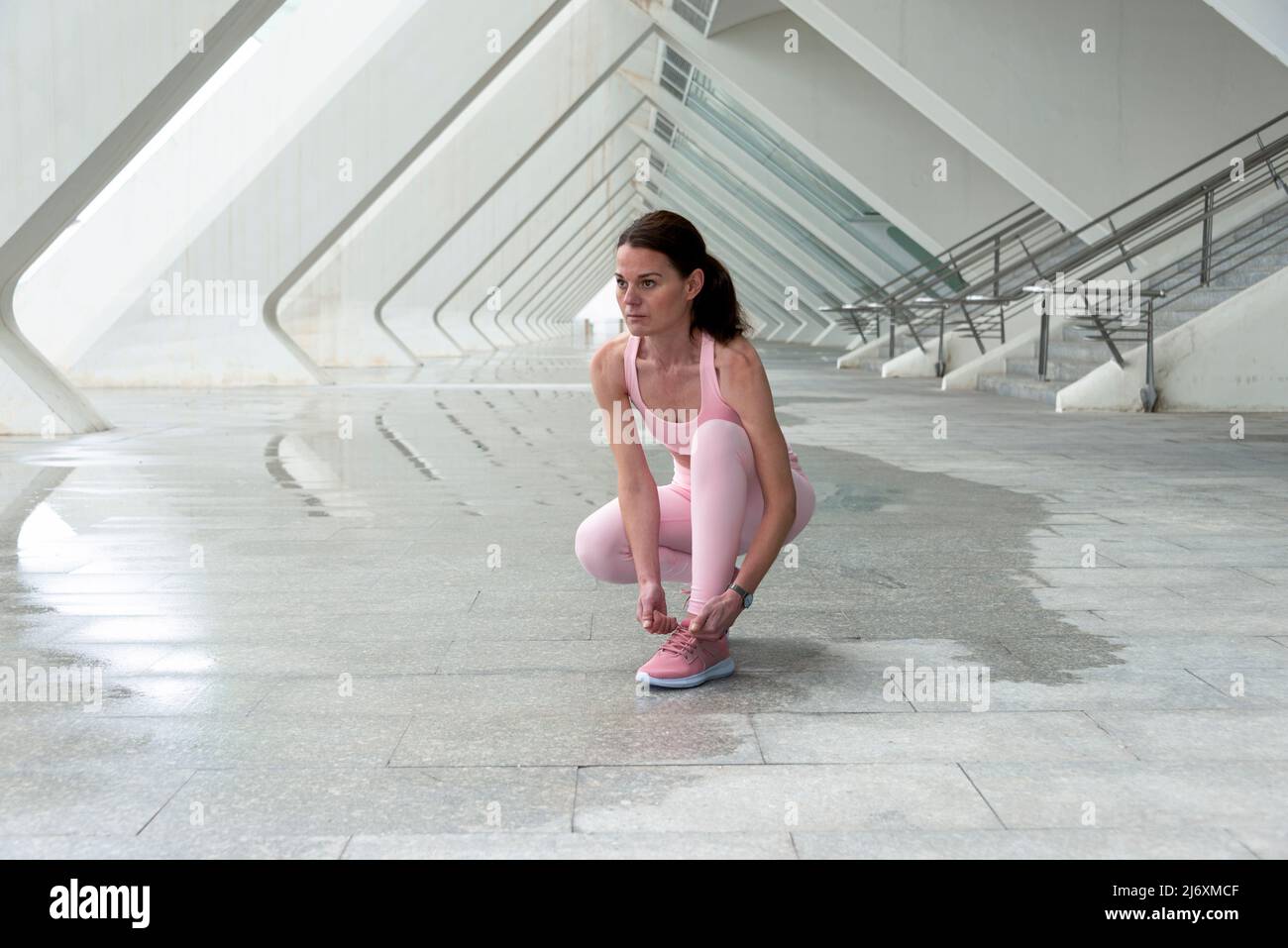 Woman runner tying here shoelaces before exercise, modern urban setting. Stock Photo