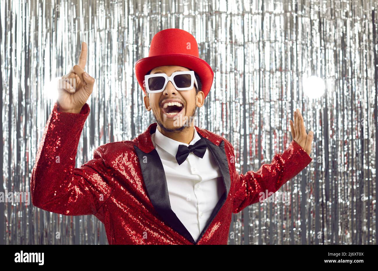 Positive funny young dark-skinned showman in shiny suit on silver foil background. Stock Photo