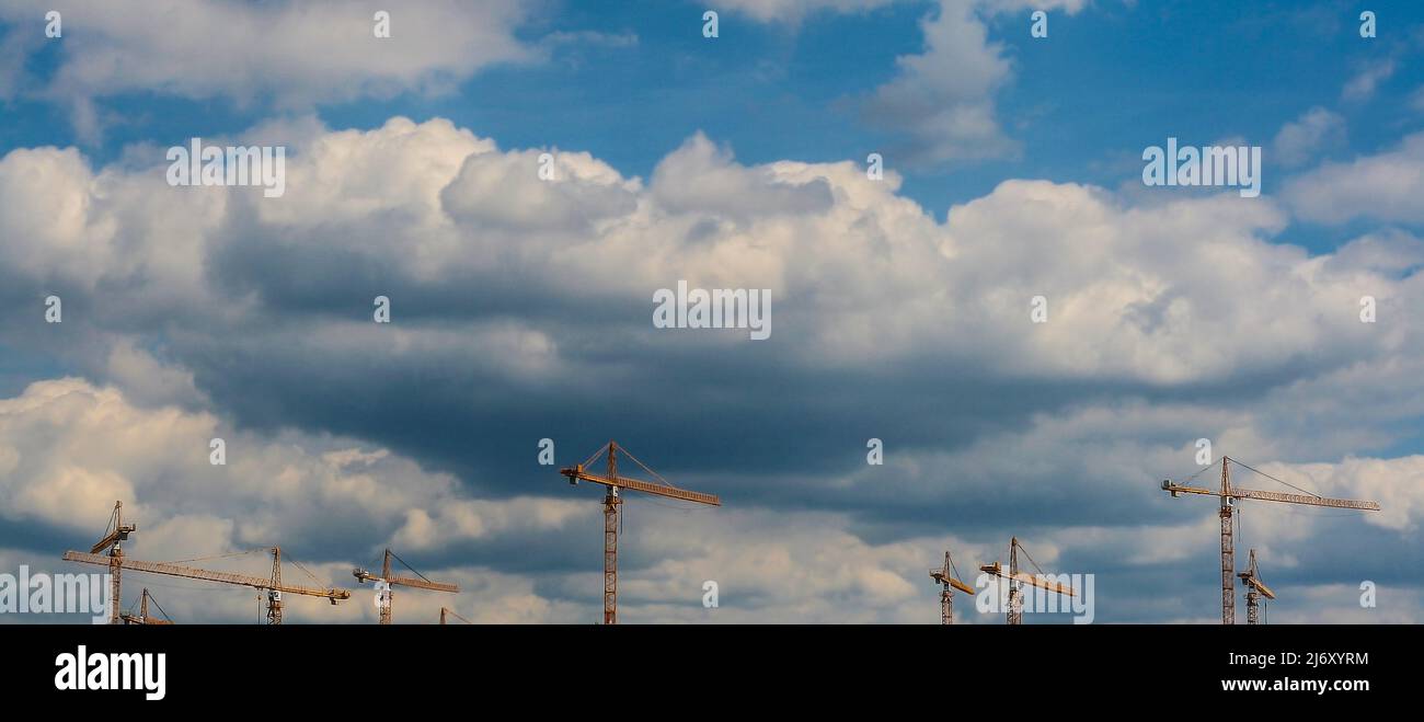 Many yellow construction tower cranes against cloudy sky Stock Photo