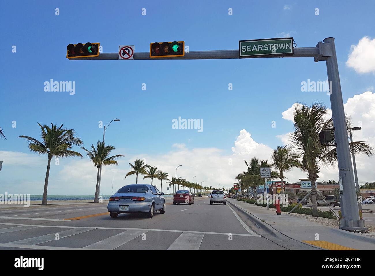 Traffic light on the highway in Miami in clear weather with sea views and white clouds. US road