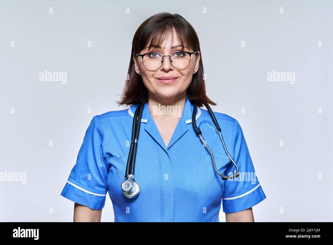 Headshot portrait of smiling middle aged nurse in blue uniform looking ...