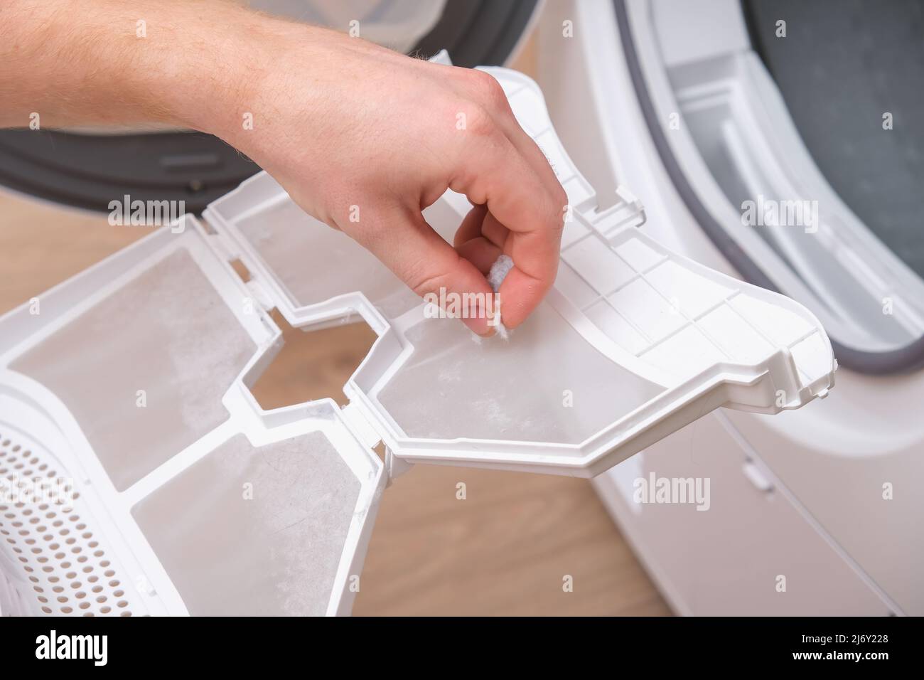 A man takes a lint filter out of the dryer and cleans it from dust, lint, hair, wool Stock Photo