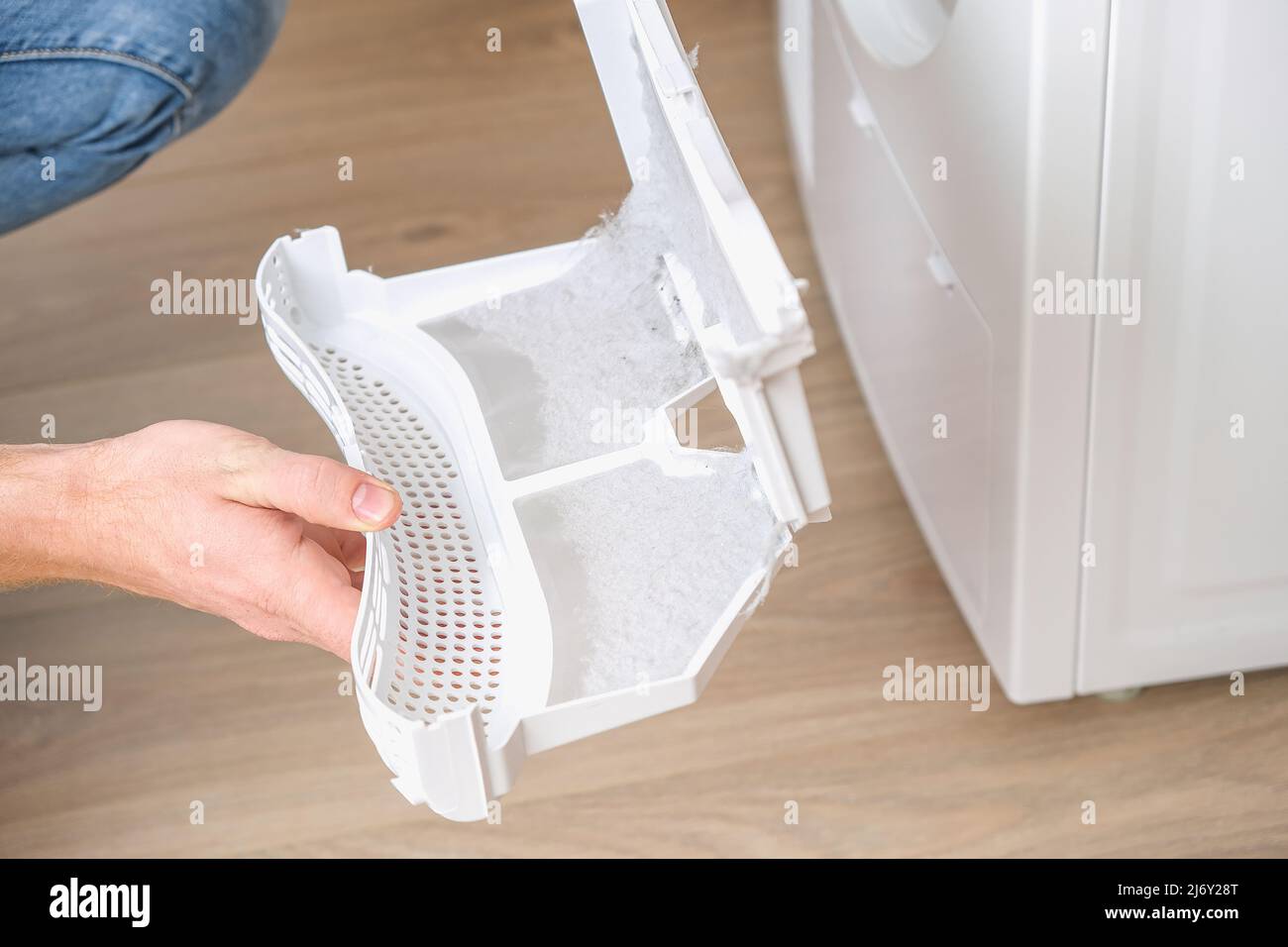 A man takes a lint filter out of the dryer and cleans it from dust, lint, hair, wool Stock Photo