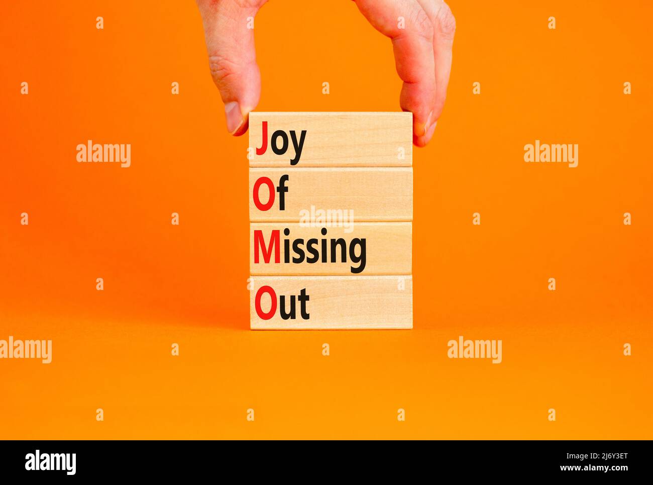 JOMO joy of missing out symbol. Concept words JOMO joy of missing out on wooden blocks on a beautiful orange background. Businessman hand. Business JO Stock Photo