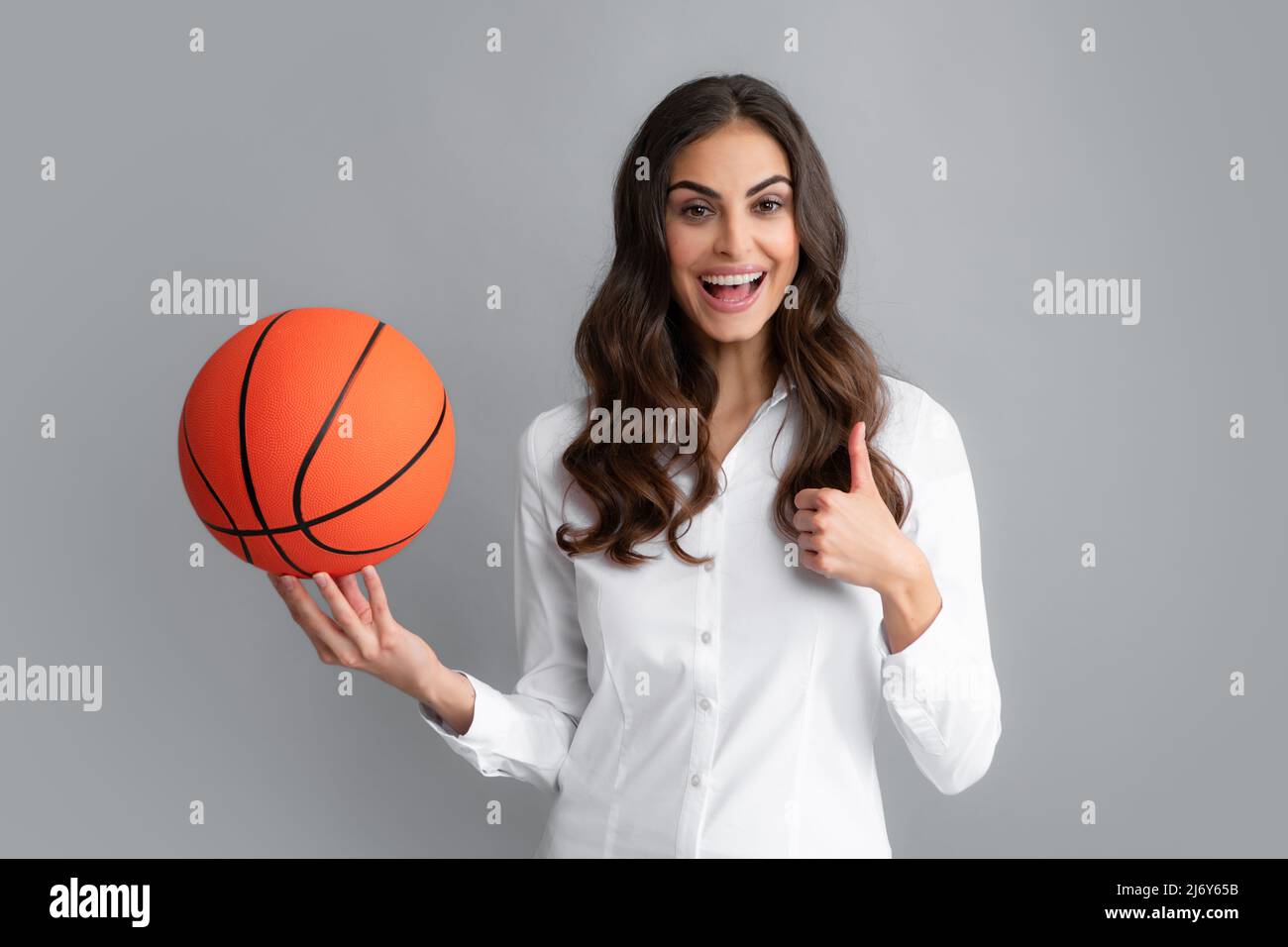 Happy woman with thumb up holding a basketball ball, isolated on gray background. Stock Photo