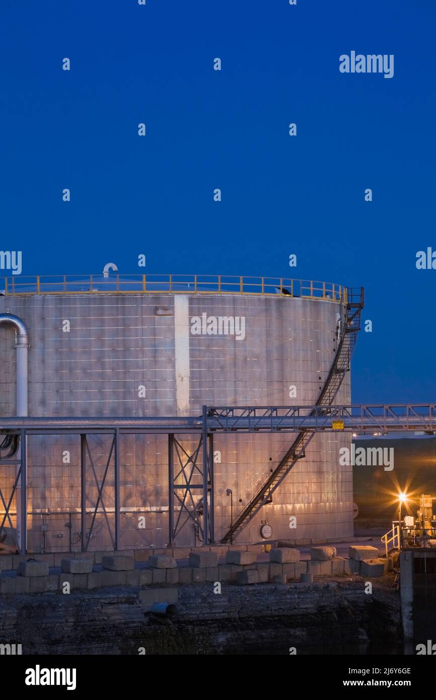 Oil storage tank at an oil and gas refinery illuminated at dusk ...