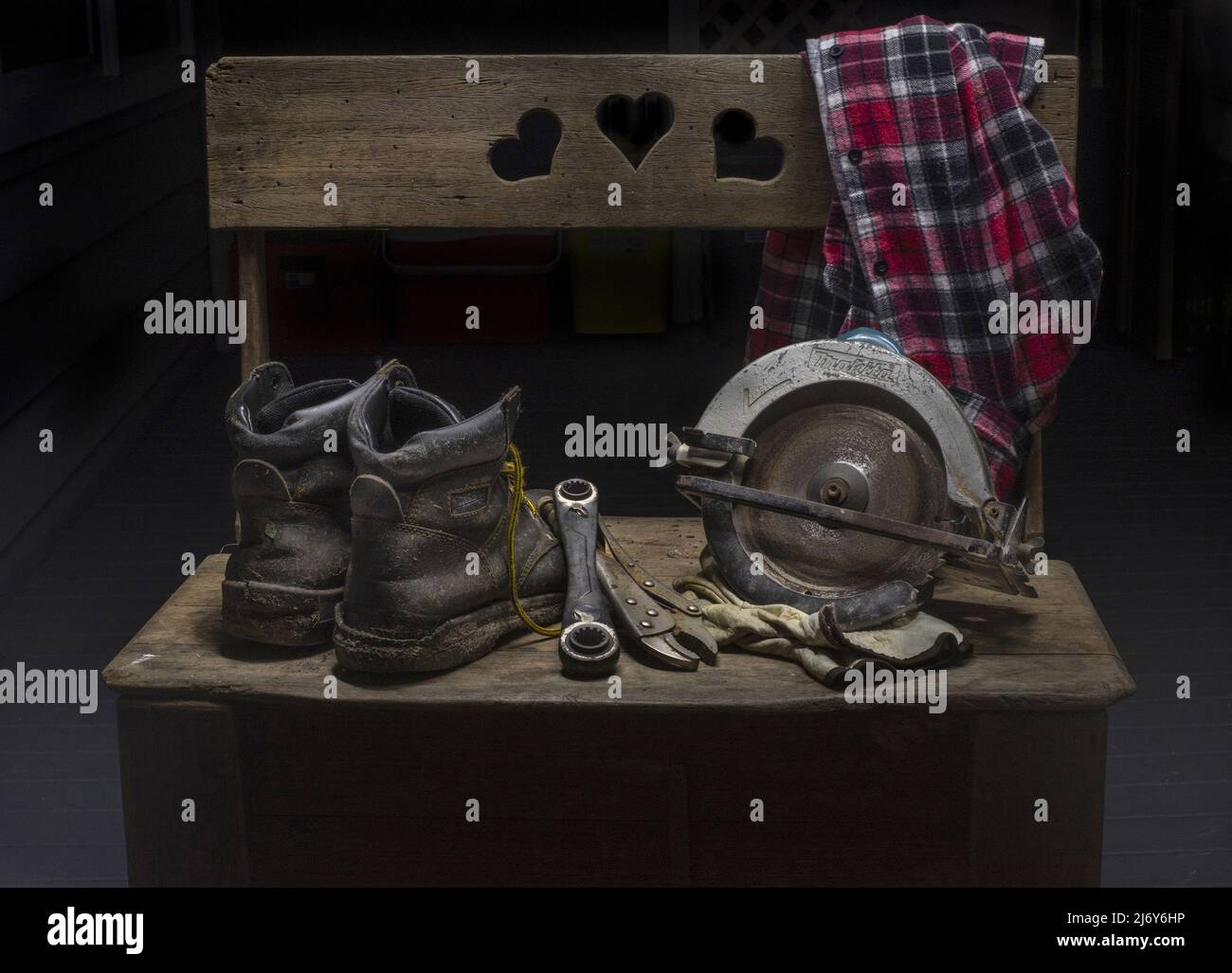 Boots, a circular saw, hand-tools and a work shirt placed on an old wooden storage box. Stock Photo