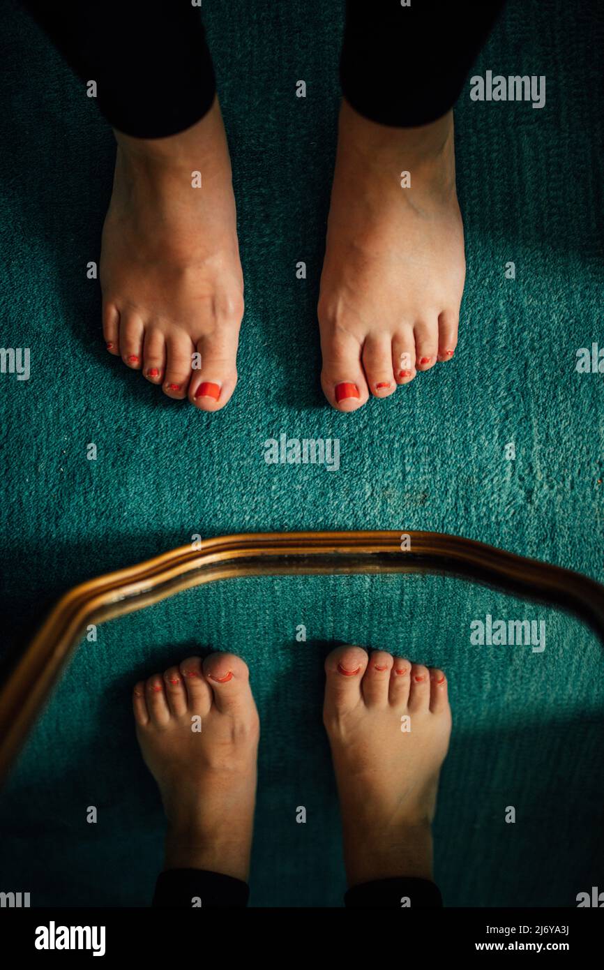 feet with red painted toenails on teal carpet and gold rim mirror Stock Photo