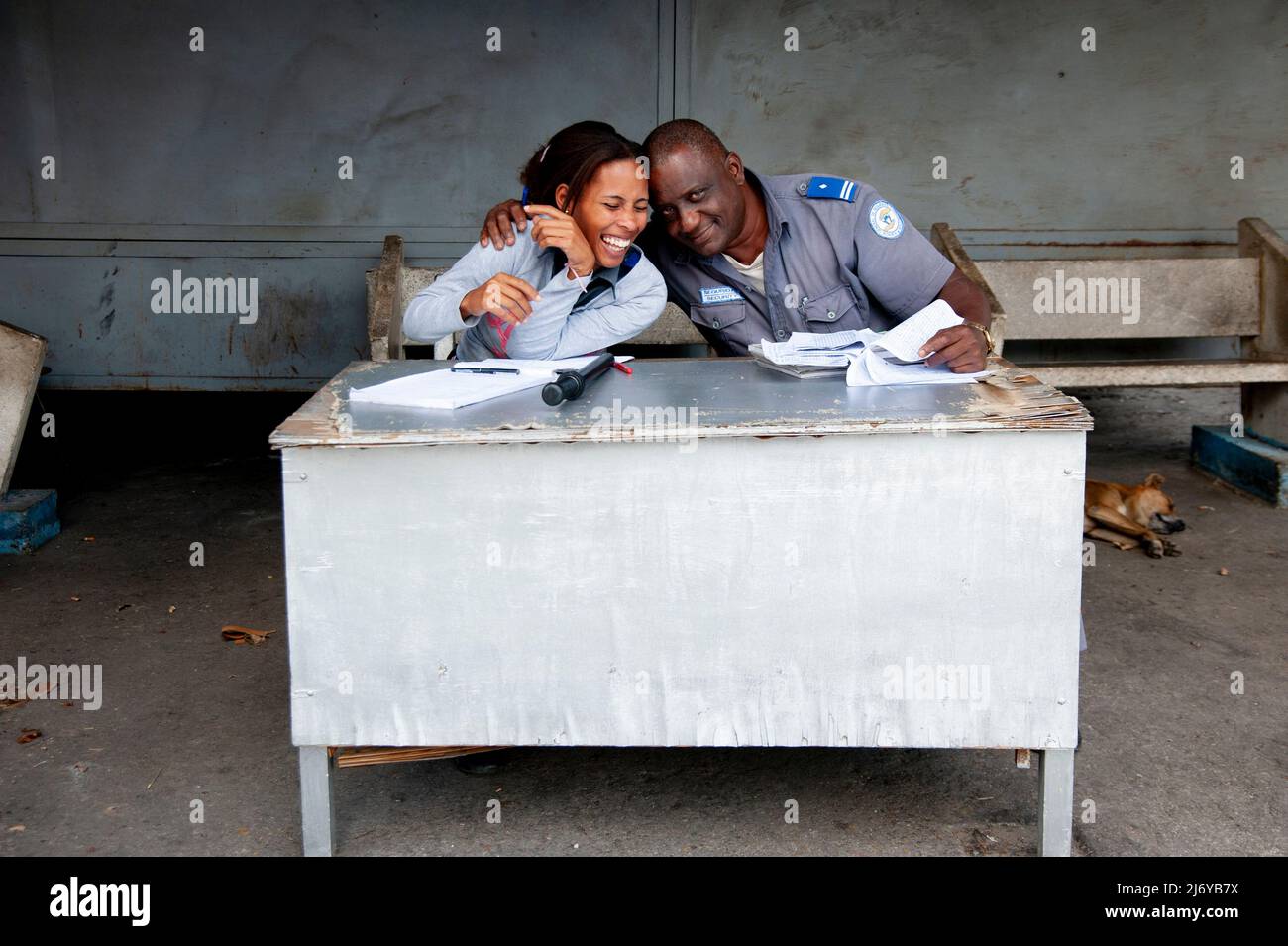 Cuban man and woman security office co-workers laugh together while working as a street dog sleeps on the ground in Havana, Cuba. Stock Photo