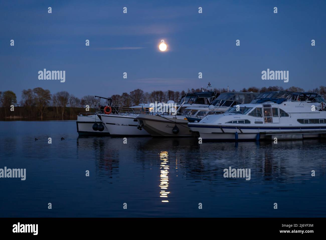 Full moon shining bright on boats and yachts in the harbor. Night at the lake in a rural area. Tranquil scene with beautiful nature. Landscape Stock Photo