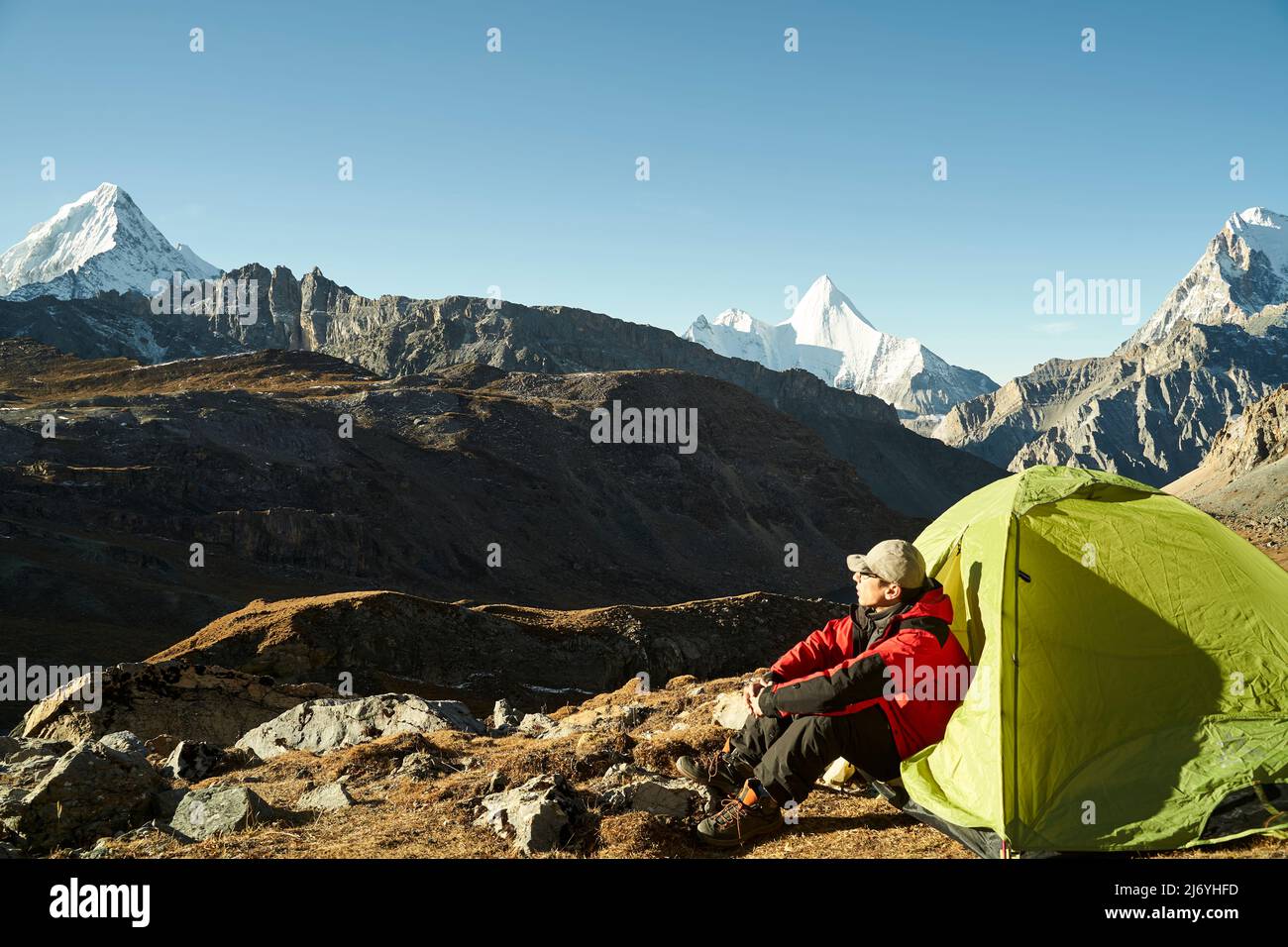 asian man male camper sitting in tent enjoying the early morning sunlight in yading national park, daocheng county, sichuan province, china Stock Photo