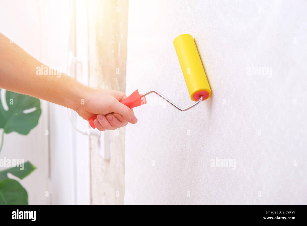 A man rolls out a canvas of white wallpaper with a suture wallpaper yellow roller. Removing air