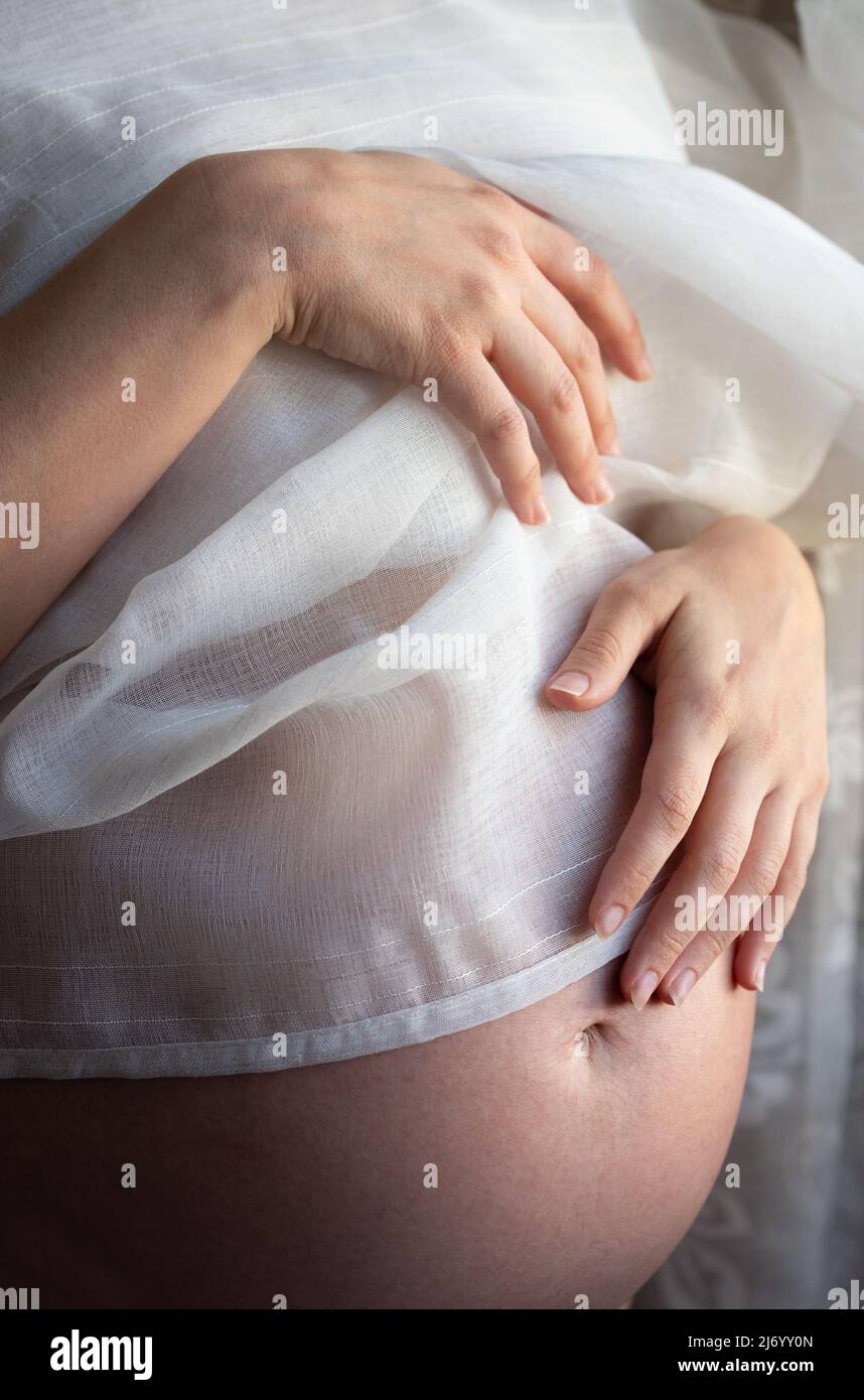 Close-up and detail shot of a pregnant woman's abdomen, whose bulging abdomen is covered with a delicate cloth Stock Photo