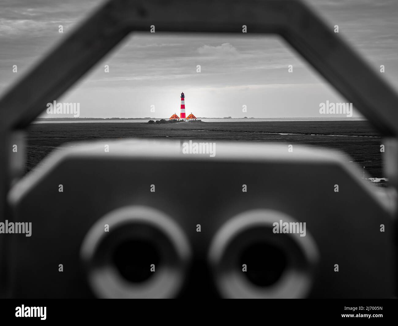 black and white photography of a pair of binoculars at westerhever dike with selective red and white colored lighthouse westerheversand in distance. Stock Photo