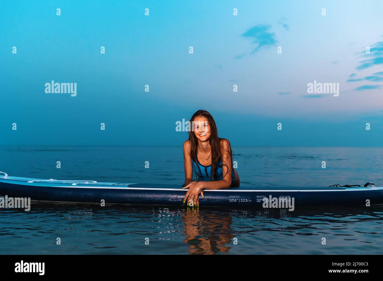 Summer sport. Portrait of young smiling tanned woman poses leaning on a sup board. Copy space. Concept of surfing. Stock Photo