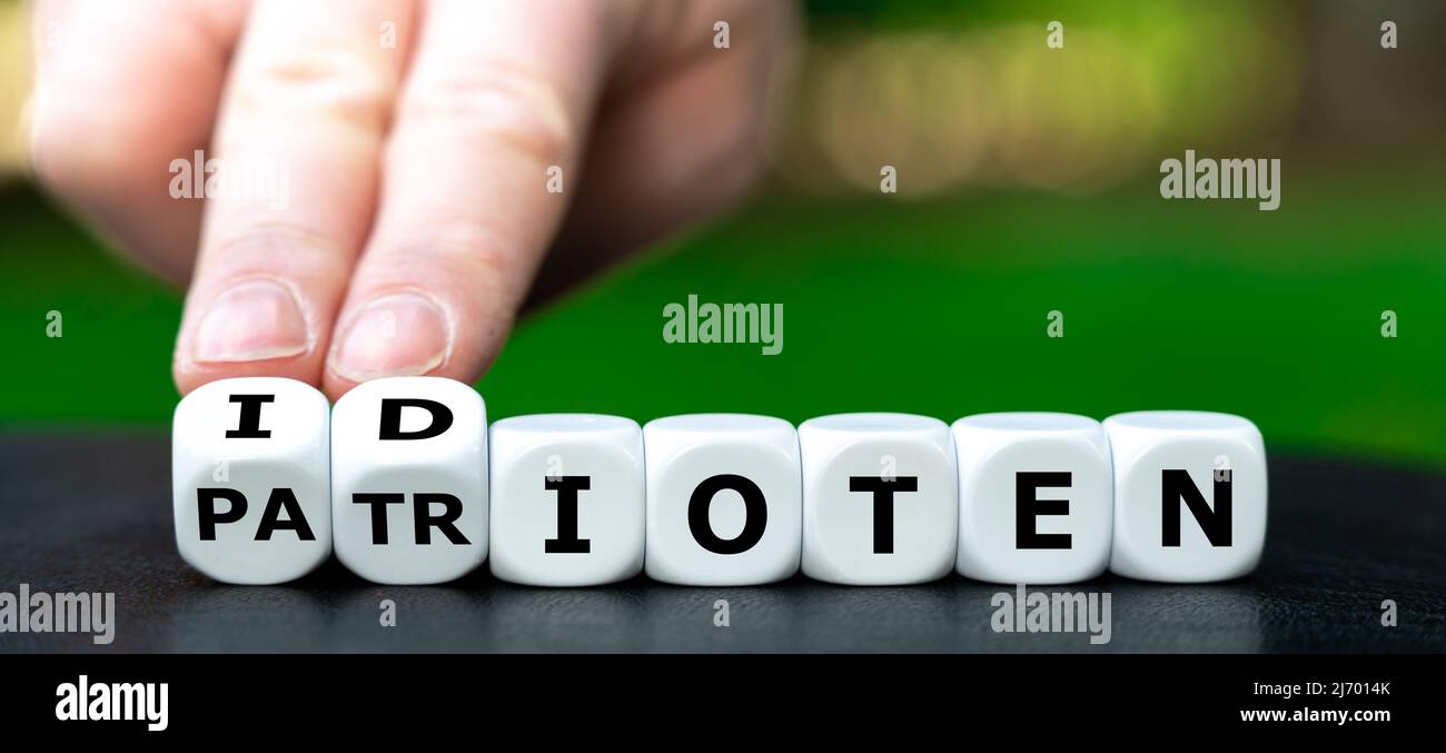 Hand turns dice and changes the German word 'Patrioten' (patriots) to 'idioten' (idiots). Stock Photo