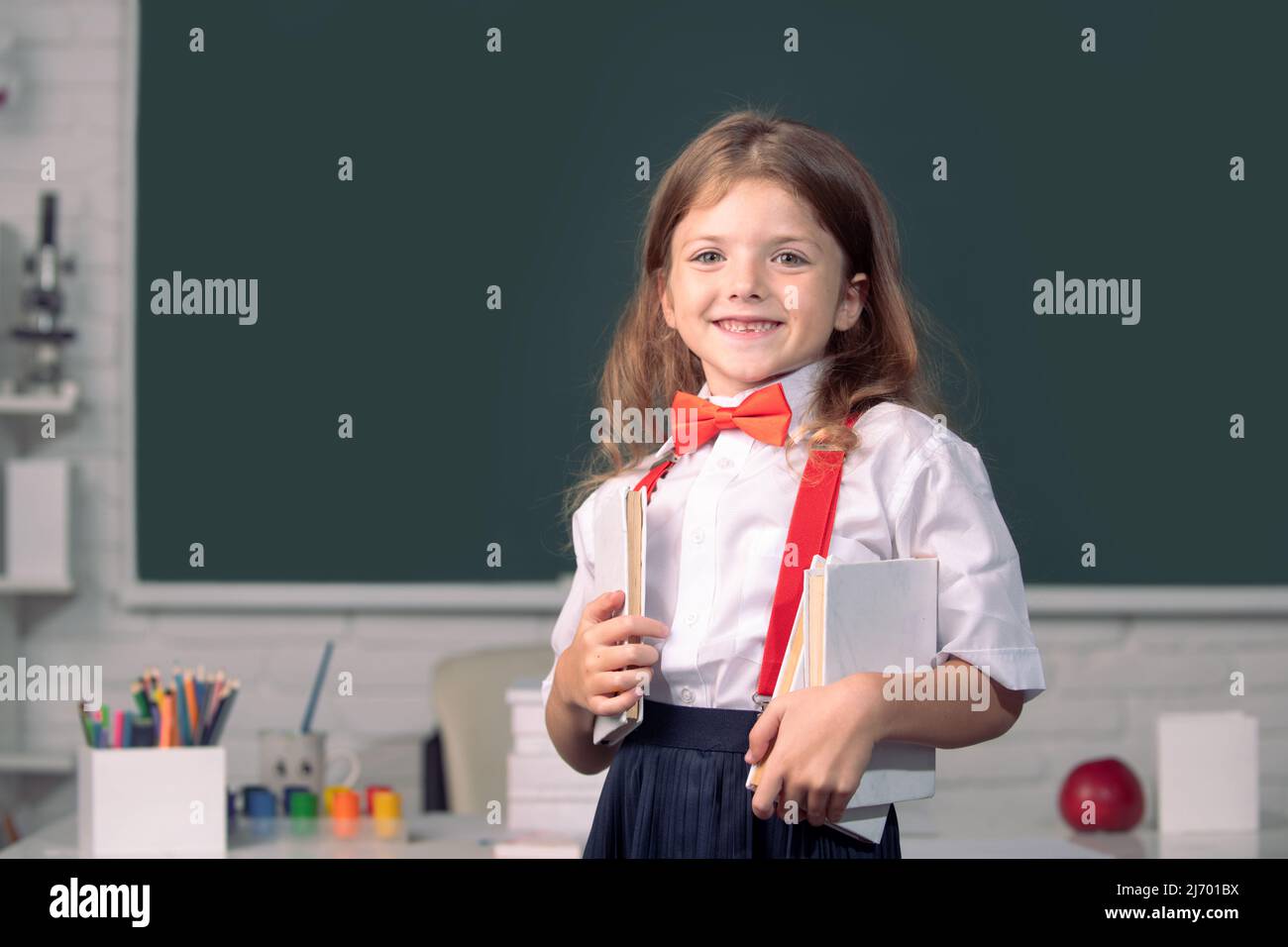 Portrait of cute, smiling girl in school uniform in classroom. Genius ...