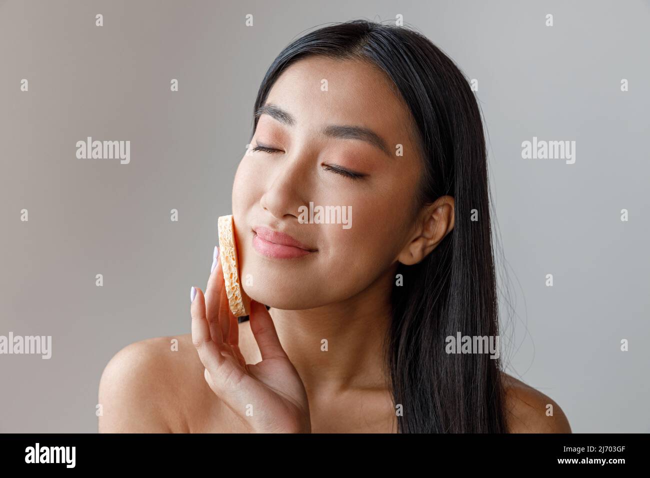Asian young woman cleaning face with cosmetic sponge Stock Photo