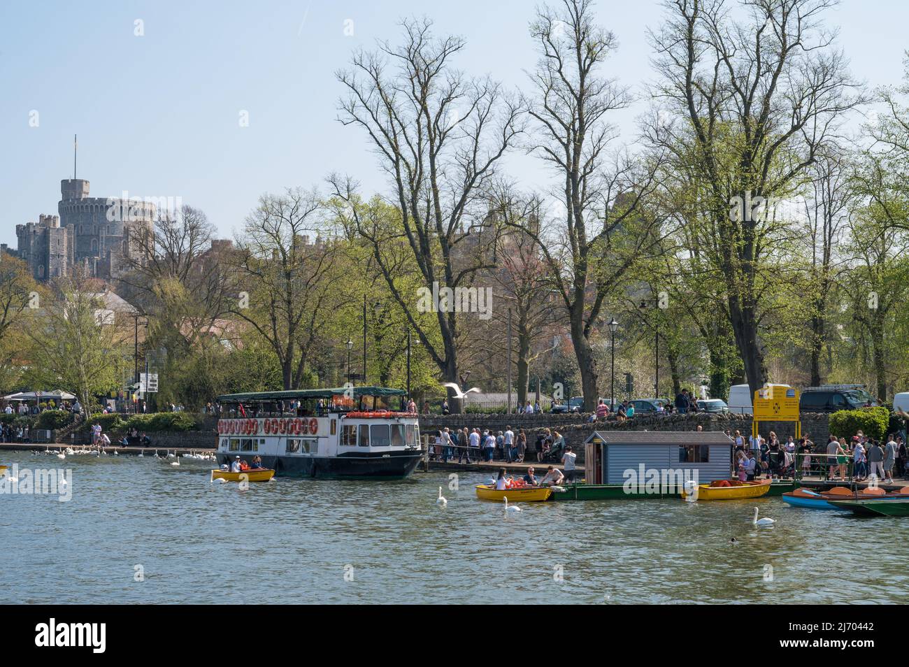 People enjoying a sunny springtime day on the Thames river path and using hire motorboats. Windsor Castle in background. England, UK. Stock Photo