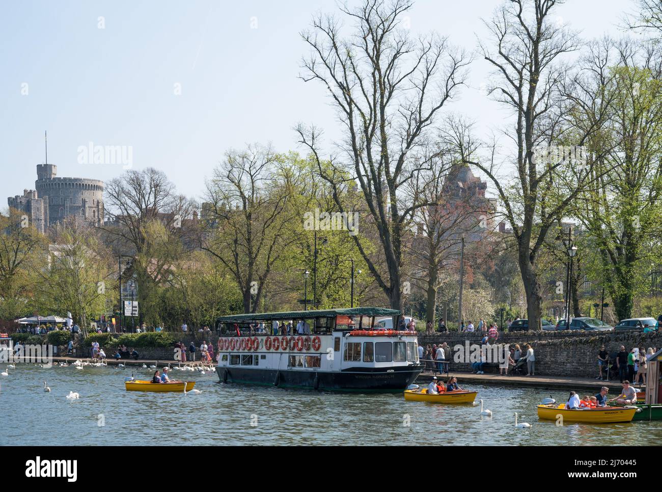 People enjoying a sunny springtime day on the Thames river path and using hire motorboats. Windsor Castle in background. England, UK. Stock Photo