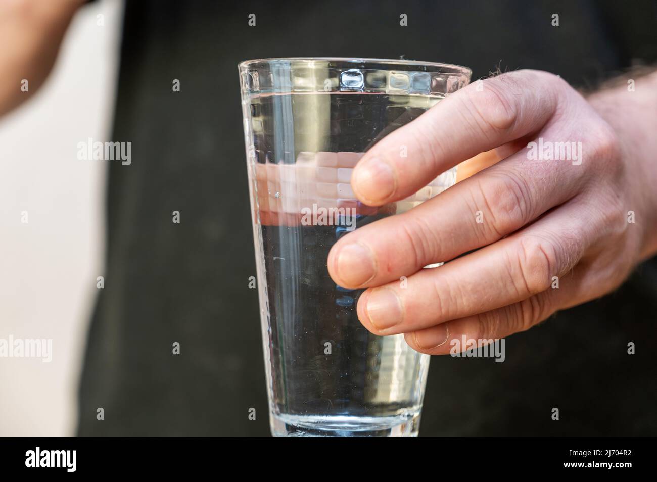 Closeup of a hand holding a tall glass of water. A mature man in a