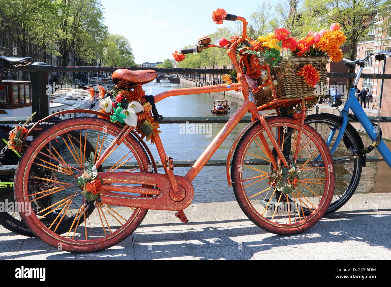 orange bike with flowers on basket parked on bridge over canal in