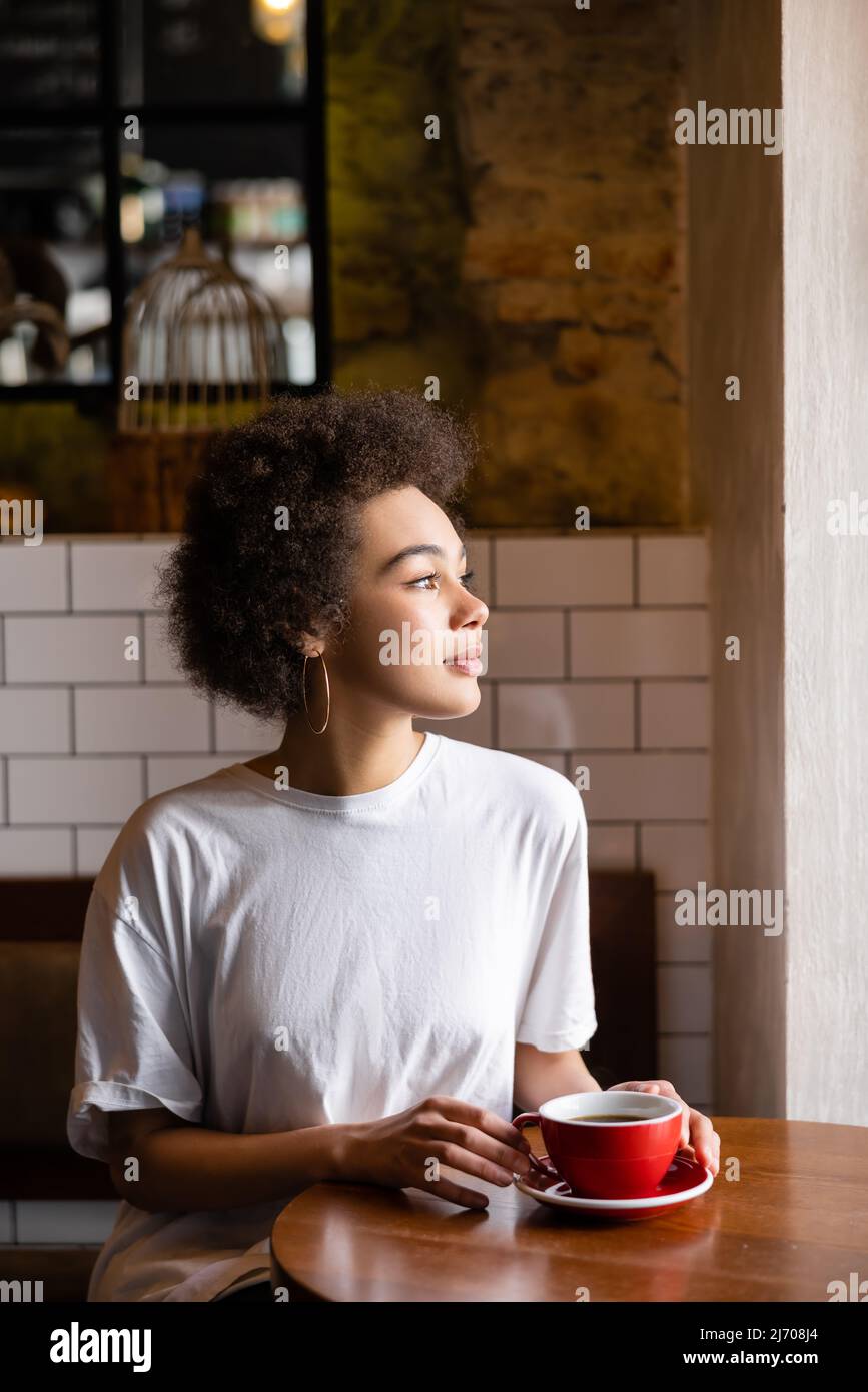 african american woman in hoop earrings and white t-shirt holding cup of coffee Stock Photo