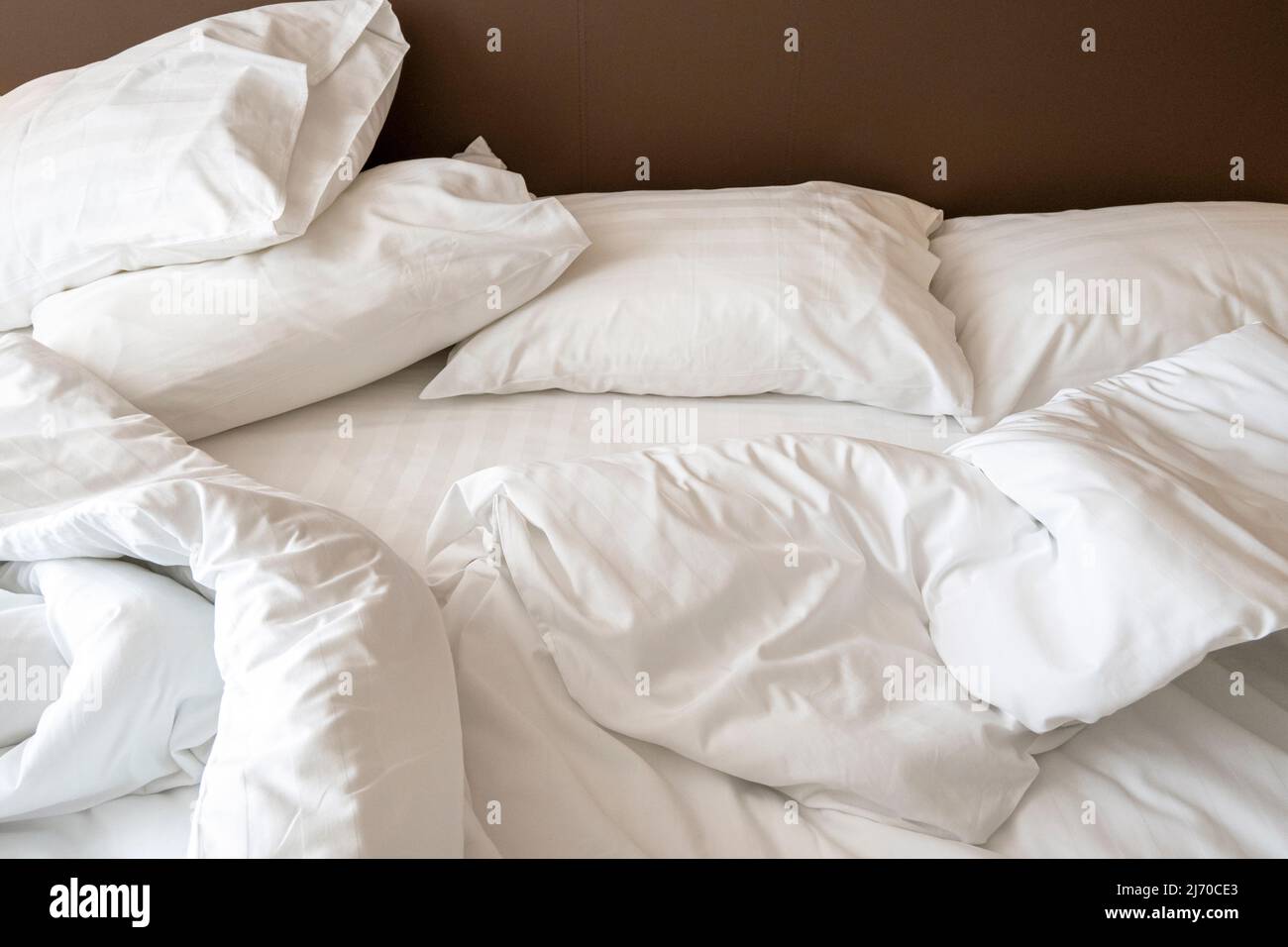 Interior of hotel room in the morning with messy bed. Crumpled white bed linen, pillows and blanket on the bed Stock Photo